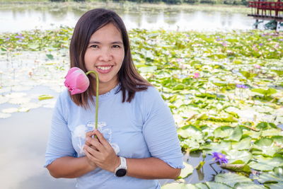 Portrait of smiling young woman holding lotus in lake with flowering plants