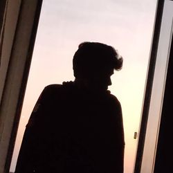 Silhouette man looking through window at sunset