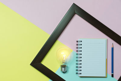 High angle view of light bulb with book and pencil on colorful table