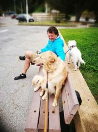 Full length of man sitting with dogs on bench at park