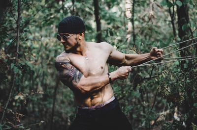 Full length of shirtless man standing in forest