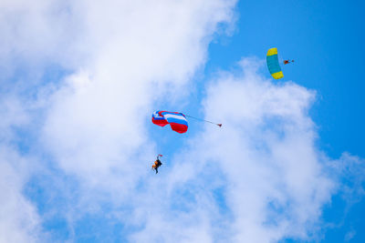 Low angle view of people paragliding against sky