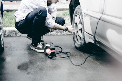 Young man inflating car tire with air pump at parking lot