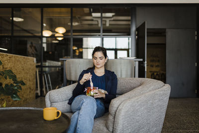 Young businesswoman eating healthy snack sitting in cafeteria at office