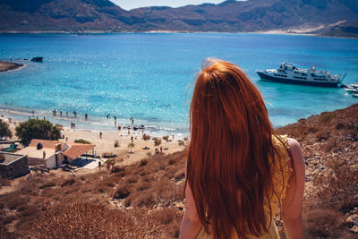 Rear view of woman with brown hair standing on mountain against beach