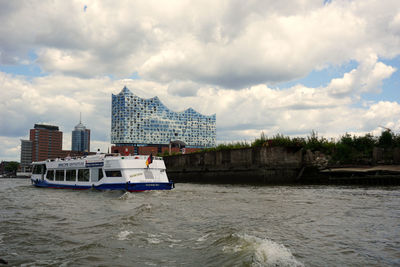 Sailboats in sea by buildings against sky