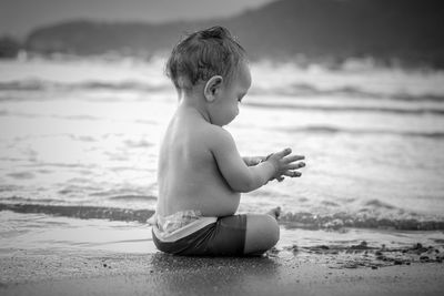 Side view of cute boy with sand playing at beach