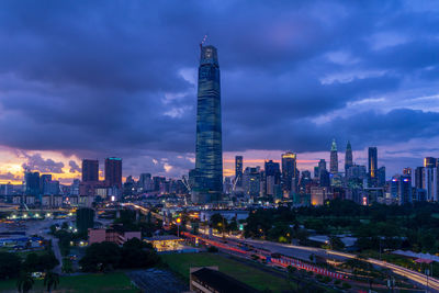 Illuminated buildings in city against cloudy sky