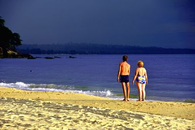Rear view of men on beach against sky