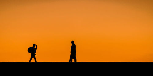 Silhouette man photographing on orange sky during sunset