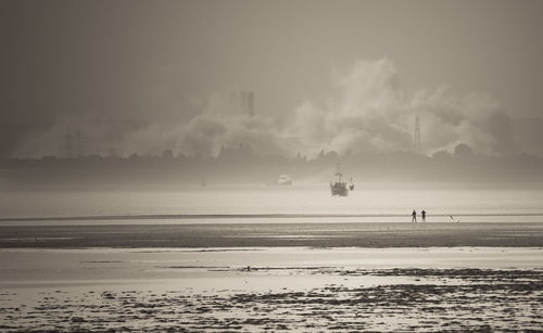 Distant view of industrial building amidst smoke seen from beach