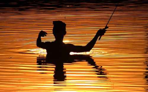 Silhouette man by lake against sky during sunset