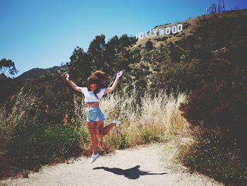 Full length of young woman jumping against hollywood sign on mountain