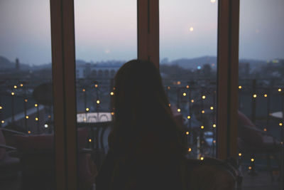 Woman looking at illuminated city against sky at dusk