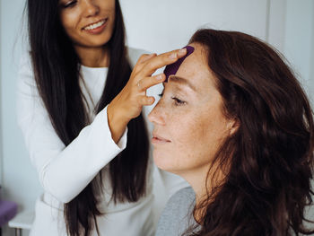 Young beautiful brunette woman with long hair in white dress taping middle age woman with curly hair 