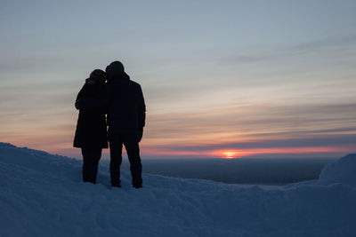 Silhouette of couple on snowy ground at sunset