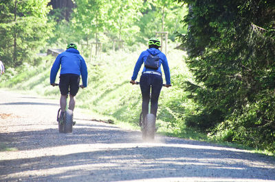 Rear view of people cycling walking on dirt road