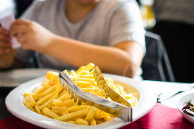 Serving tongs on french fries in plate with man sitting at table in restaurant