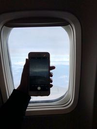 Cropped image of hand holding airplane window against sky