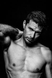 Shirtless man standing against black background and looking at the camera