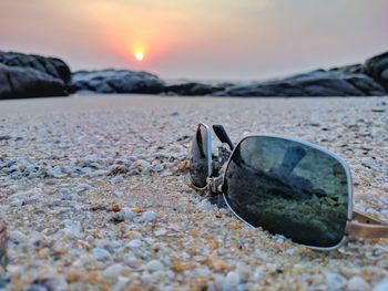 Close-up of sunglasses on beach against sky during sunset