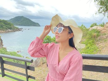 Woman wearing sunglasses standing by railing against water