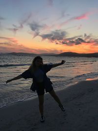 Full length portrait of woman standing on beach against sky during sunset