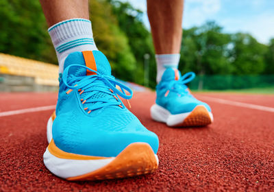 Athlete wearing bright blue running shoes on red stadium track during training