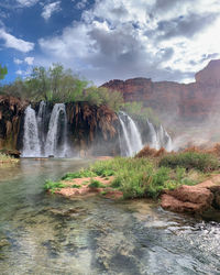 Low angle view of turquoise waterfall in havasupai against cloudy sky