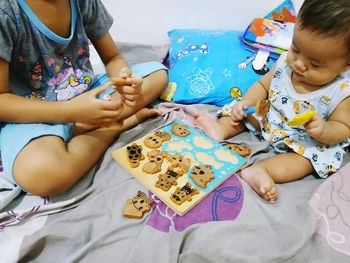 Siblings playing with toys on bed at home