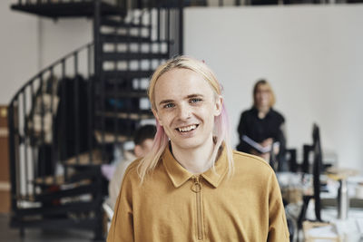 Portrait of smiling non-binary computer programmer with dyed long hair at tech start-up office
