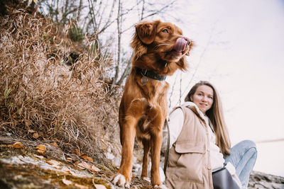 Young woman and dog retriever walks on river shore at autumn season