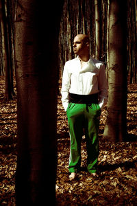 Full length of man standing by tree trunk in forest