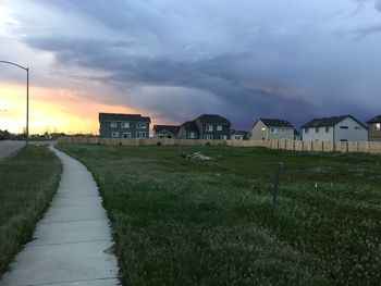 Empty road by grassy field against cloudy sky