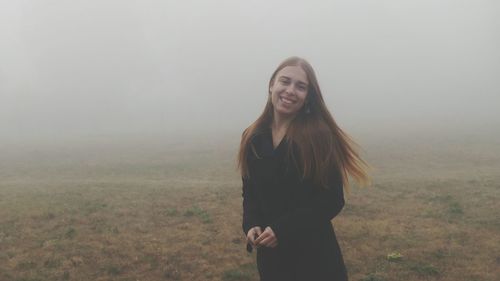 Beautiful young woman standing in foggy weather