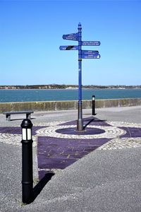 Information sign on road by sea against clear sky