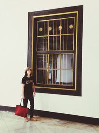 Portrait of young woman standing against window