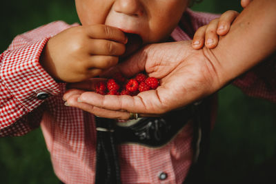 Child eating raspberries from parent's hand at farm wearing lederhosen