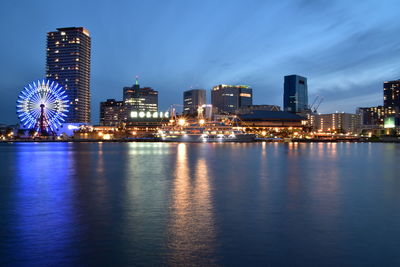 Illuminated city by river against sky at night