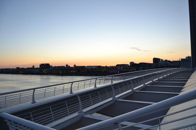 Bridge over river by buildings against sky during sunset
