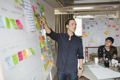 Businessman showing whiteboard and explaining colleagues during meeting in office