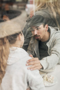 View of man consoling woman in cafe though glass