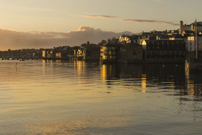 Sea by cityscape against sky during sunset