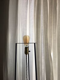 Close-up of electric lamp hanging against window at home
