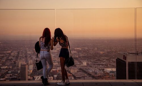 Woman with arms outstretched against cityscape during sunset