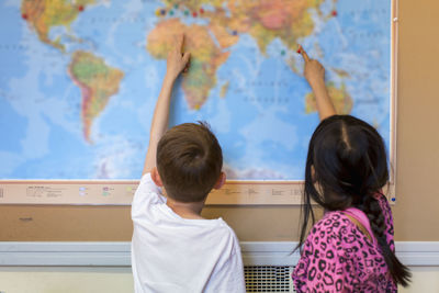 Two children looking at world map in classroom