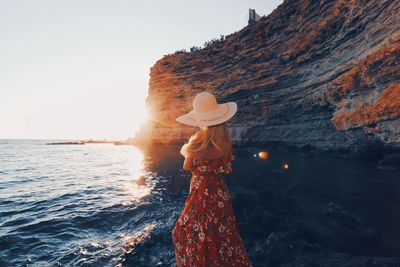 Man standing on rock by sea against sky