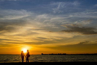 Silhouette couple standing on shore at beach against sky during sunset