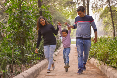 Full length of parents walking with son on footpath at park