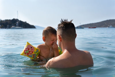 Dad and son are playing in the sea. father teaches son to dive. child covers his nose with his hand